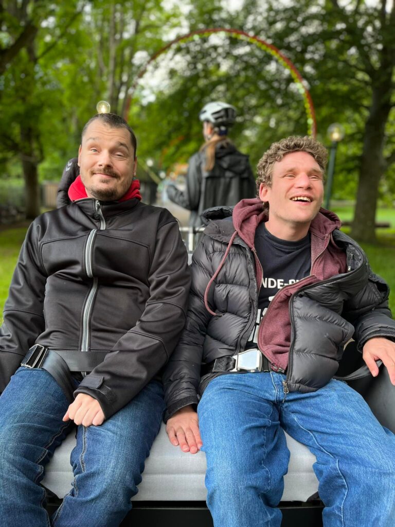 To personer siddende på en cykel i grønne omgivelser.