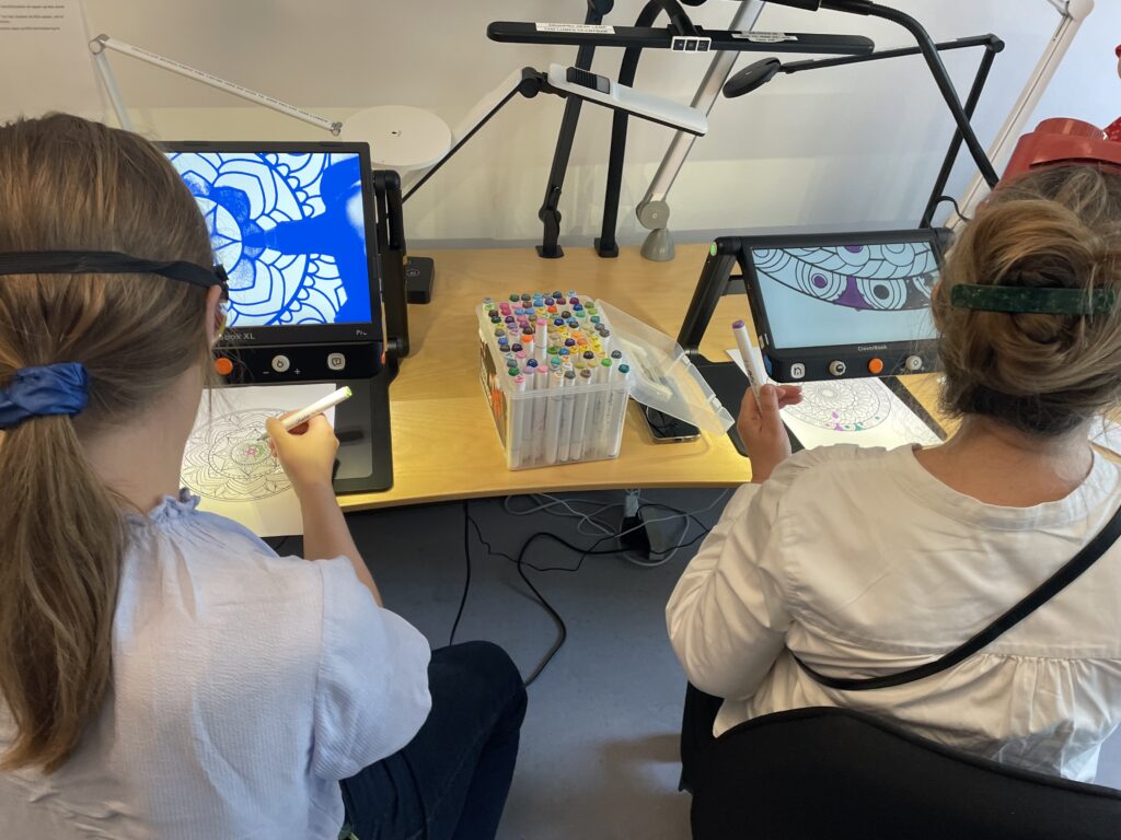 To gæster prøver at farvelægge tegning med under CCTV med simulationsbriller på.