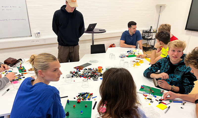 Unge ved bord fyldt med Lego der snakker sammen.