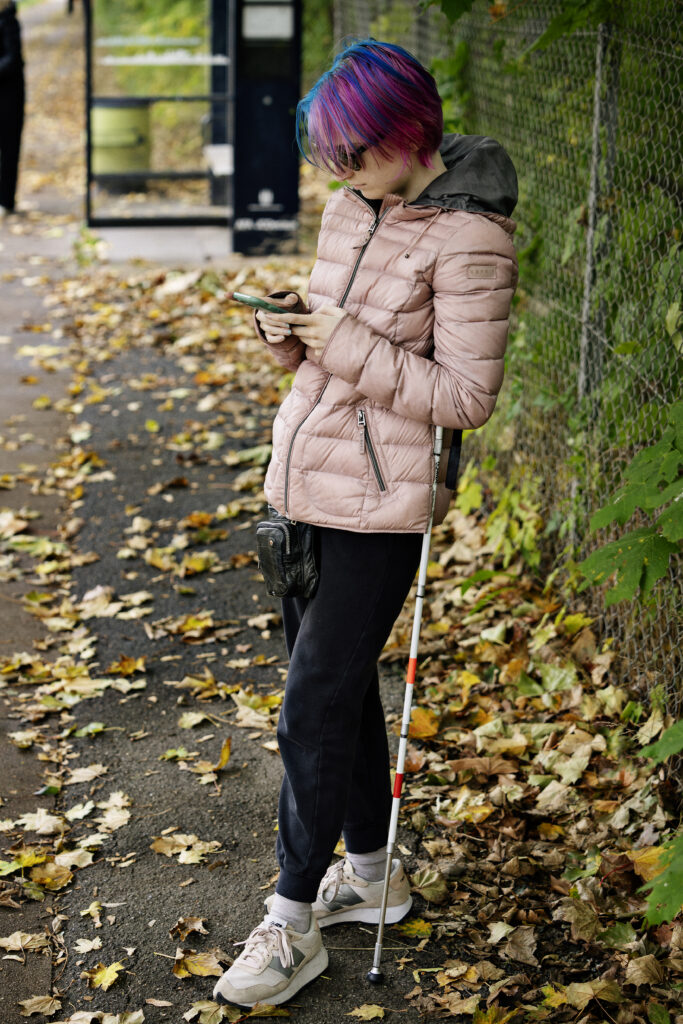 Ung pige står ved busstoppestedet med sin telefon og lænder sig mod stokken